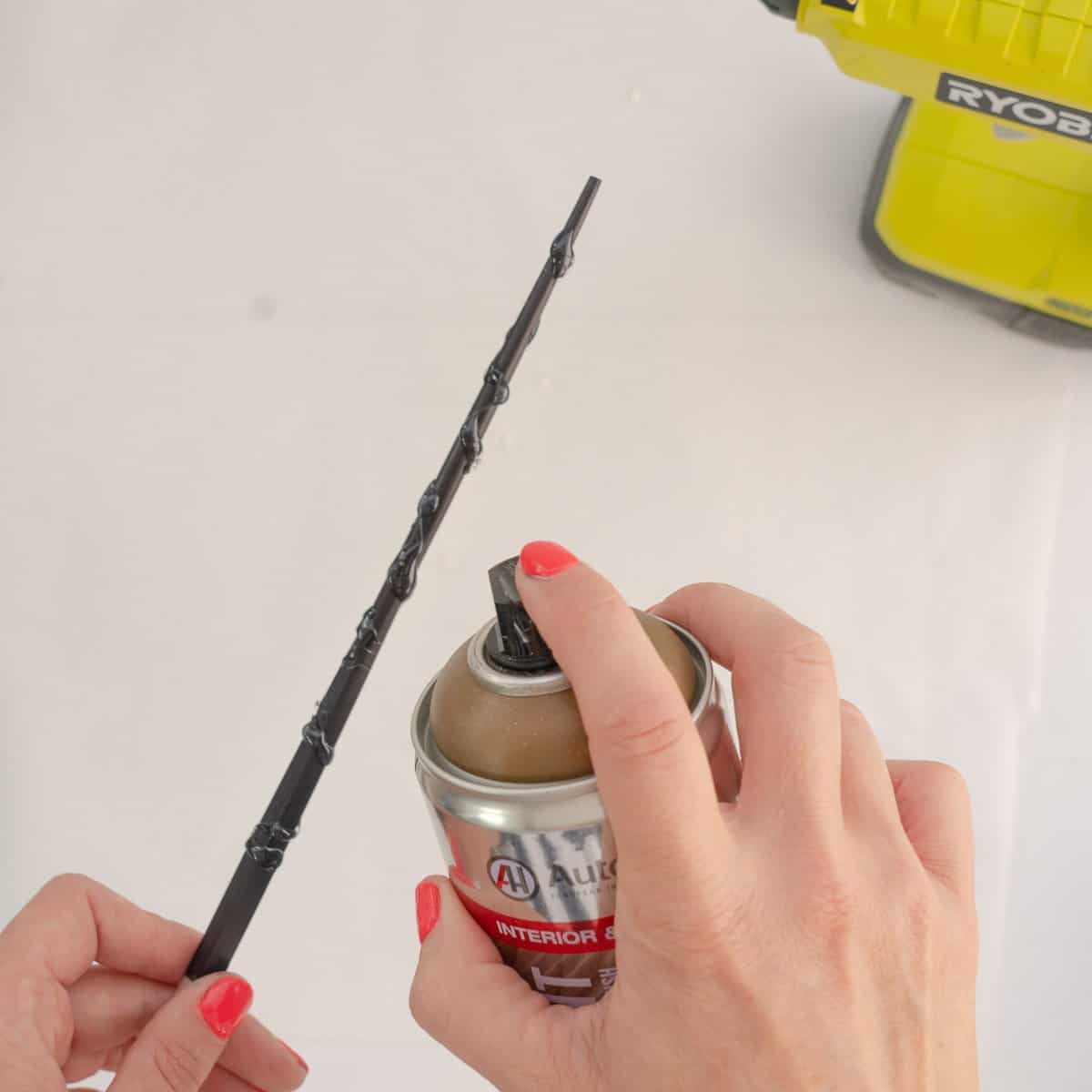 A glue covered chopstick being sprayed with metallic gold spray paint. 