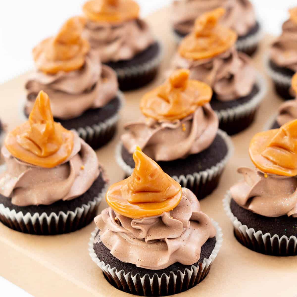 Chocolate cupcakes topped with chocolate buttercream and a caramel cupcake topper in the shape of a sorting hat from harry potter.