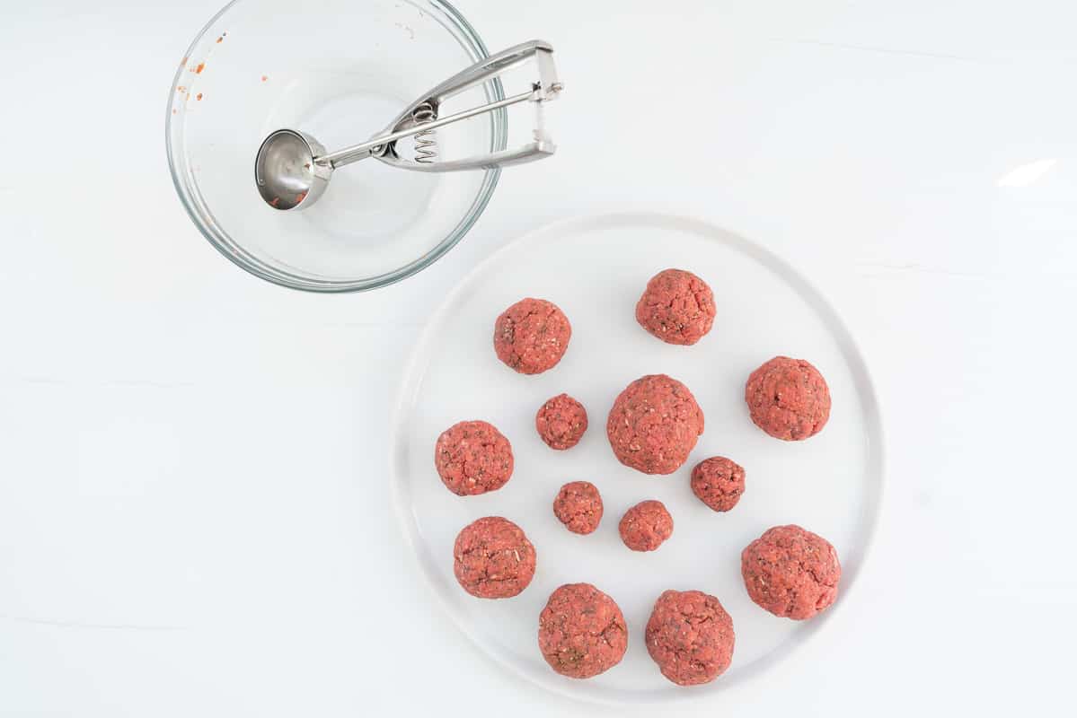 Different sized balls of hamburger mix rolled into balls, resting on a round white plate.