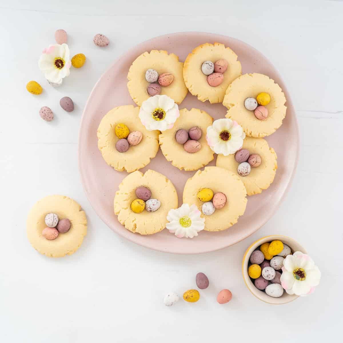9 vanilla cookies decorated with cadbury mini eggs on a pink plate.