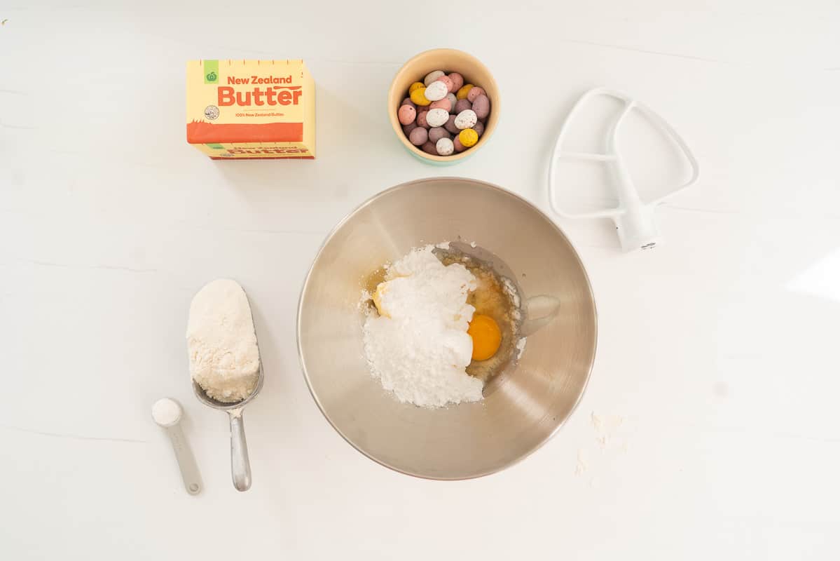a stainless steel mixing bowl of icing sugar, butter, egg and vanilla ready to be creamed.