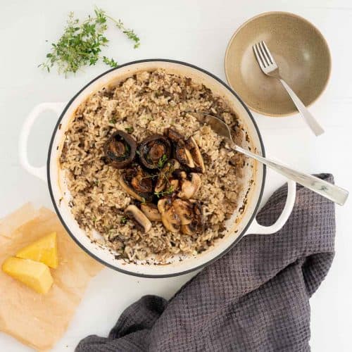 A large dish filled with mushroom risotto, topped with sliced mushrooms and garnished with thyme leaves.