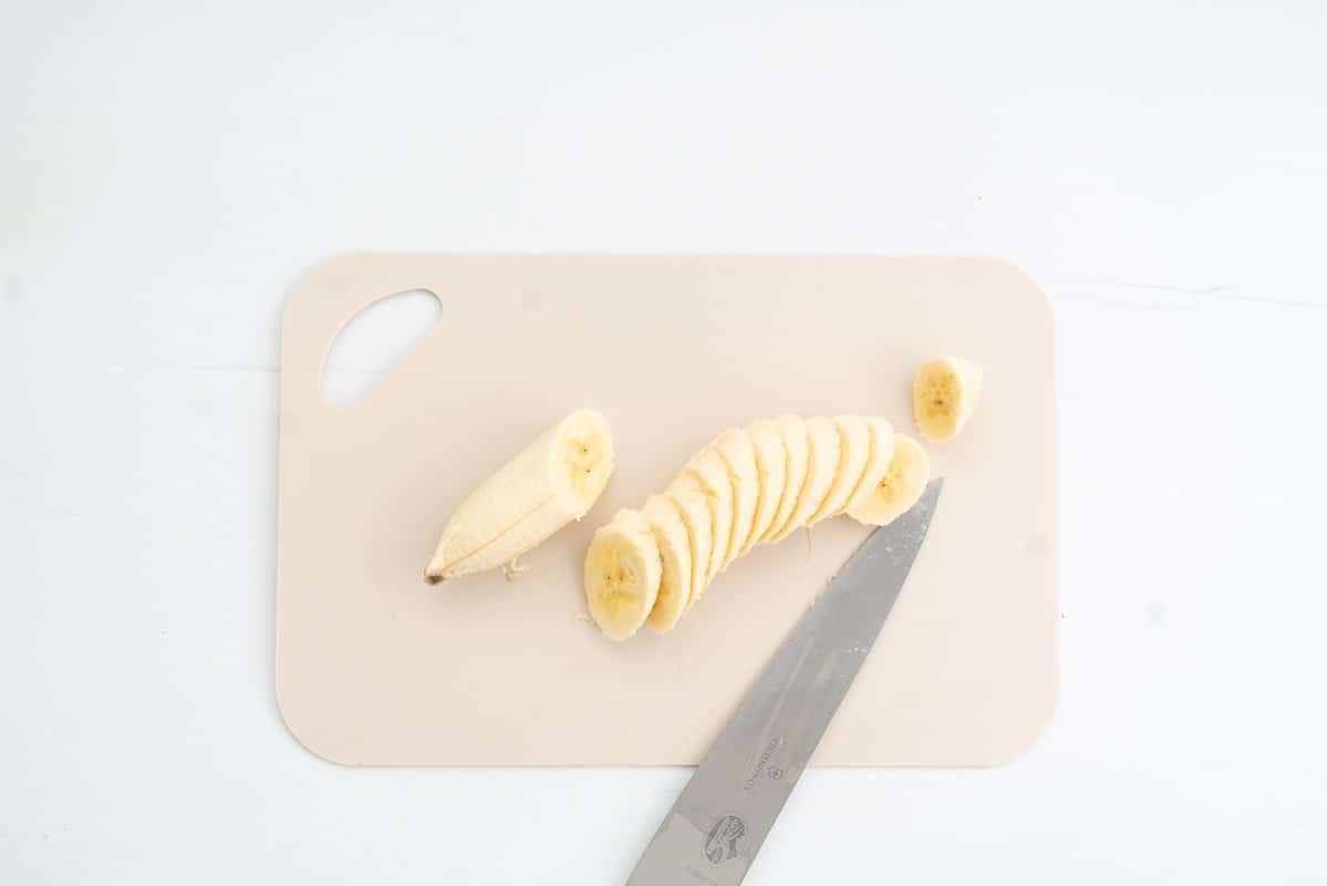 A banana sliced at an angle on a small cream chopping board.
