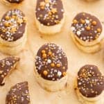 Frozen banana slices covered in chocolate and decorated with gold and silver sprinkles.