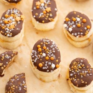 Frozen banana slices covered in chocolate and decorated with gold and silver sprinkles.