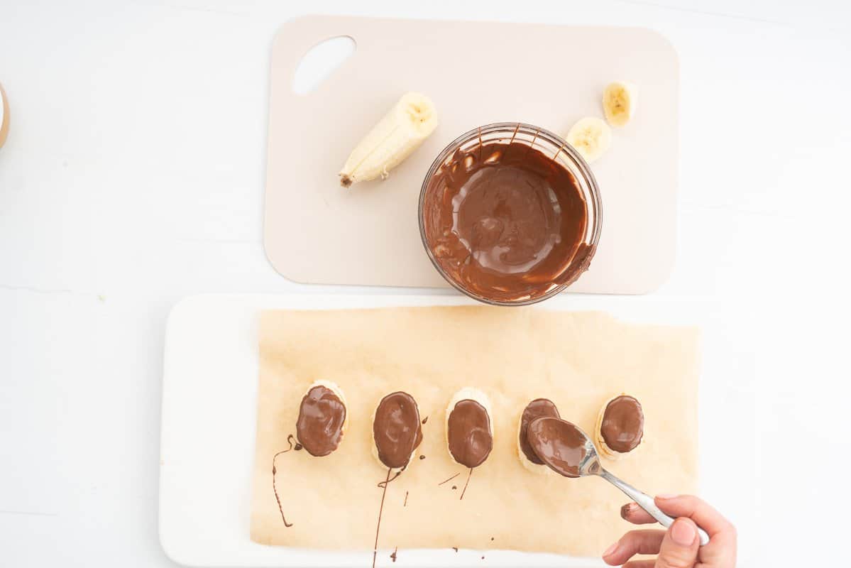 Melted chocolate being spooned on to banana slices.