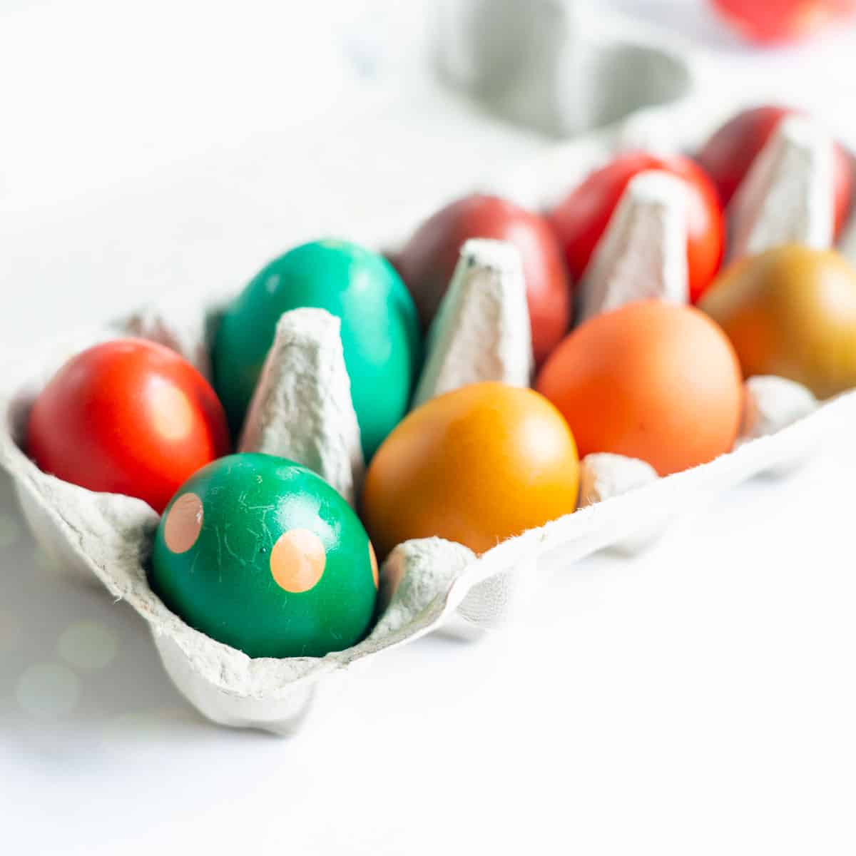 Coloured eggs in an egg carton on a white bench top.