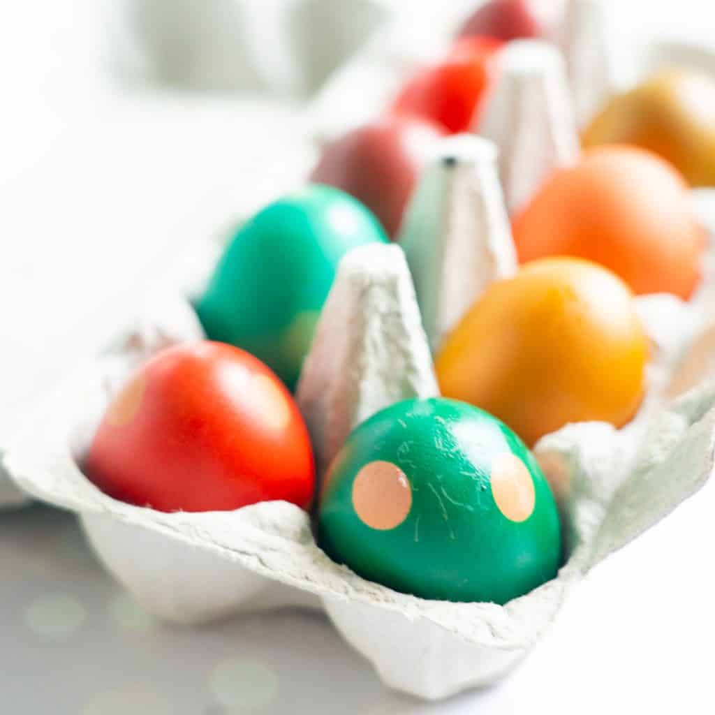 Coloured eggs in an egg carton on a white bench top.