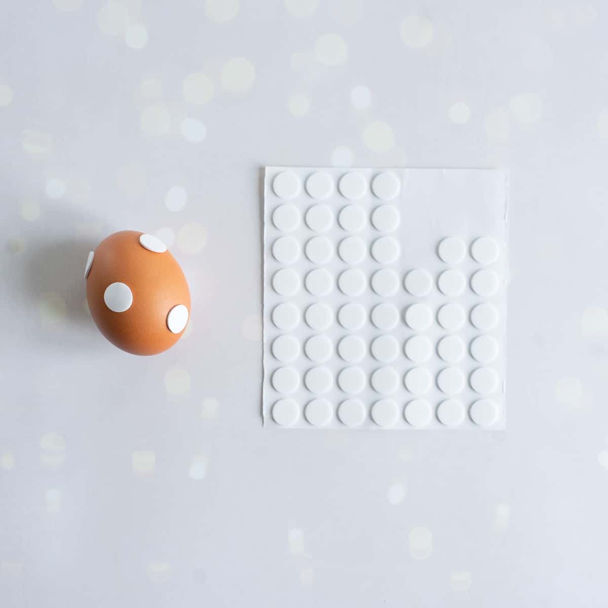 A brown shelled egg with white round stickers on it to create a polka dot pattern.