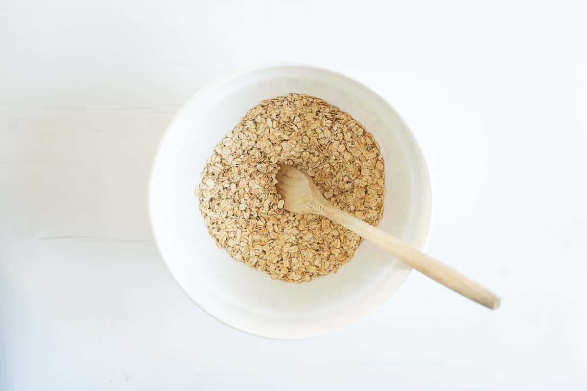 A white ceramic mixing bowl containing rolled oats and cinnamon. 