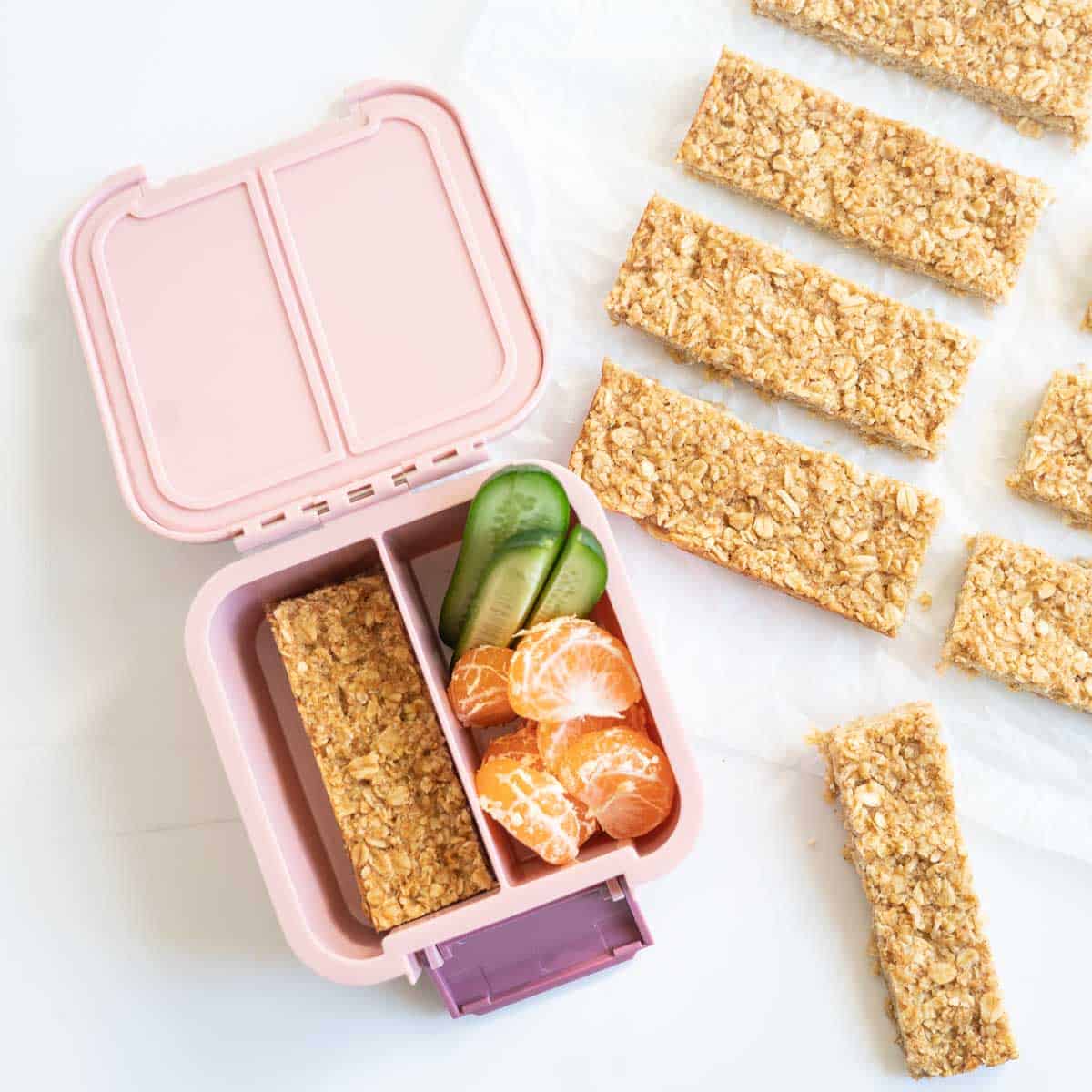 Oatmeal bars packed in to a pink lunch box with cucumber and mandarin segments