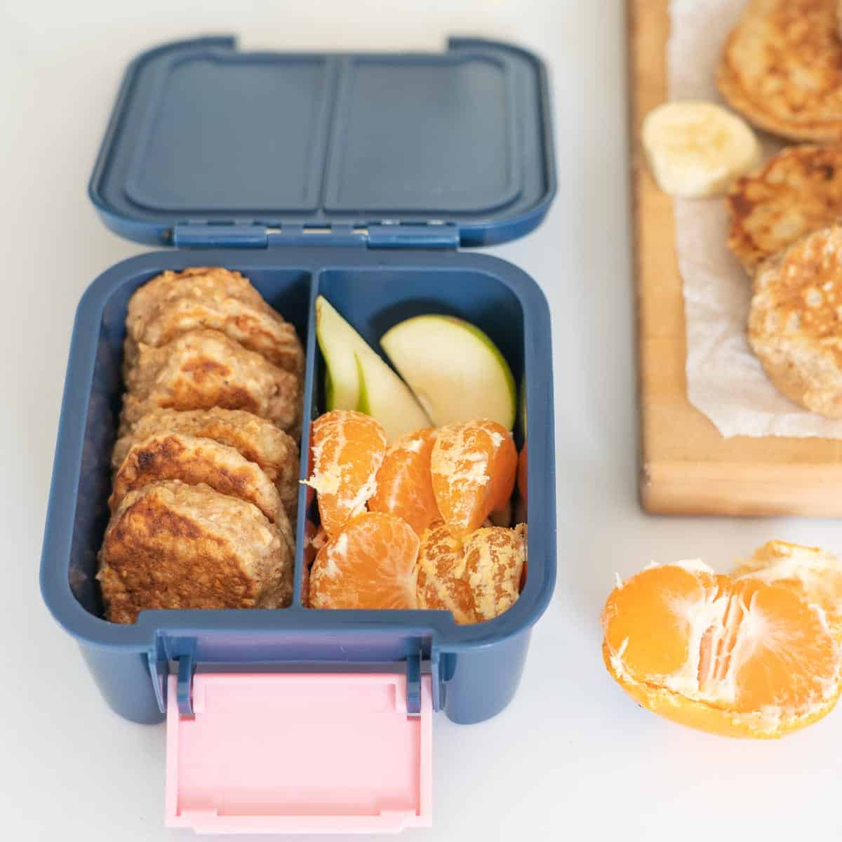 A dark blue bento box packed with pikelets, mandarin segments and pear slices. 
