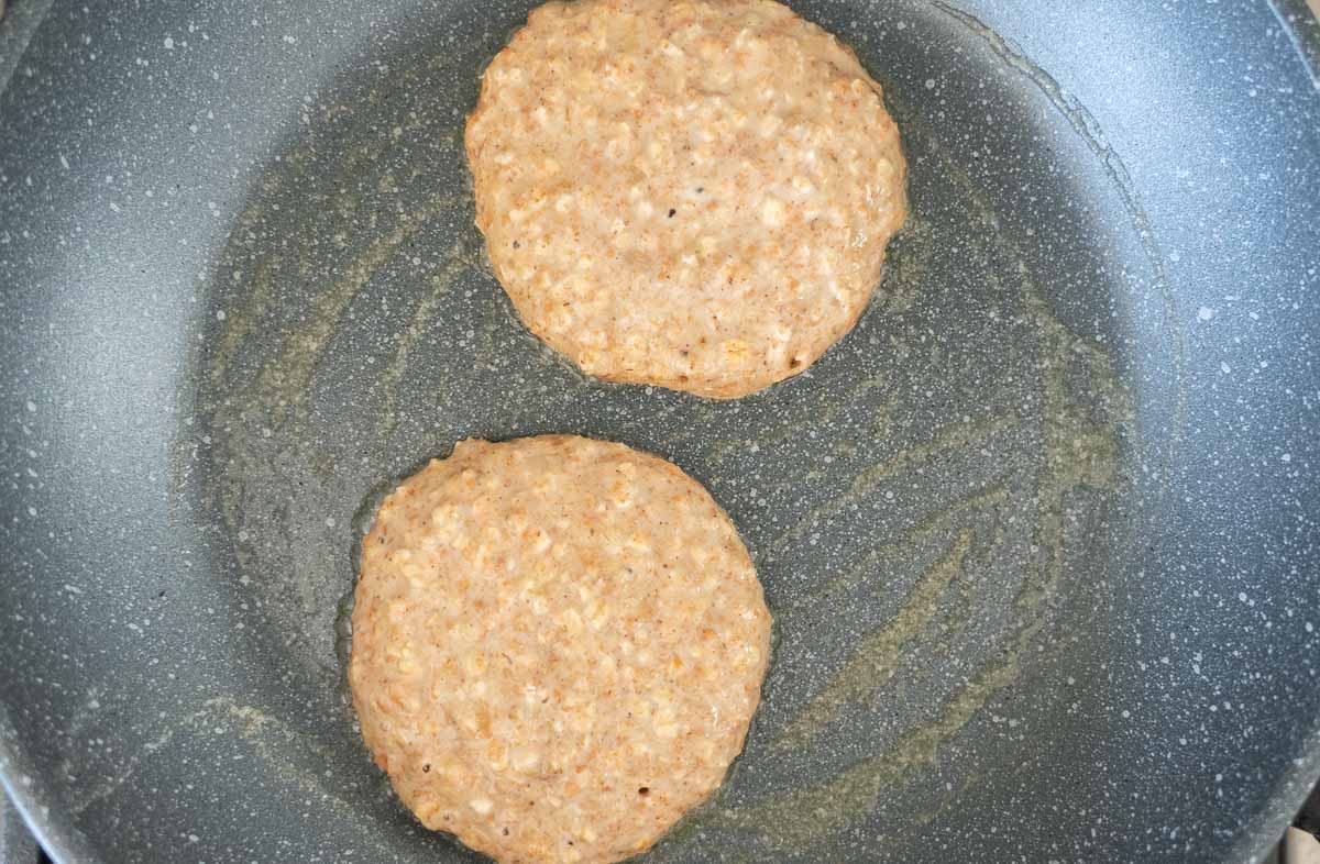 bubbles beginning to form on the surface of pikelets cooking in a frying pan.