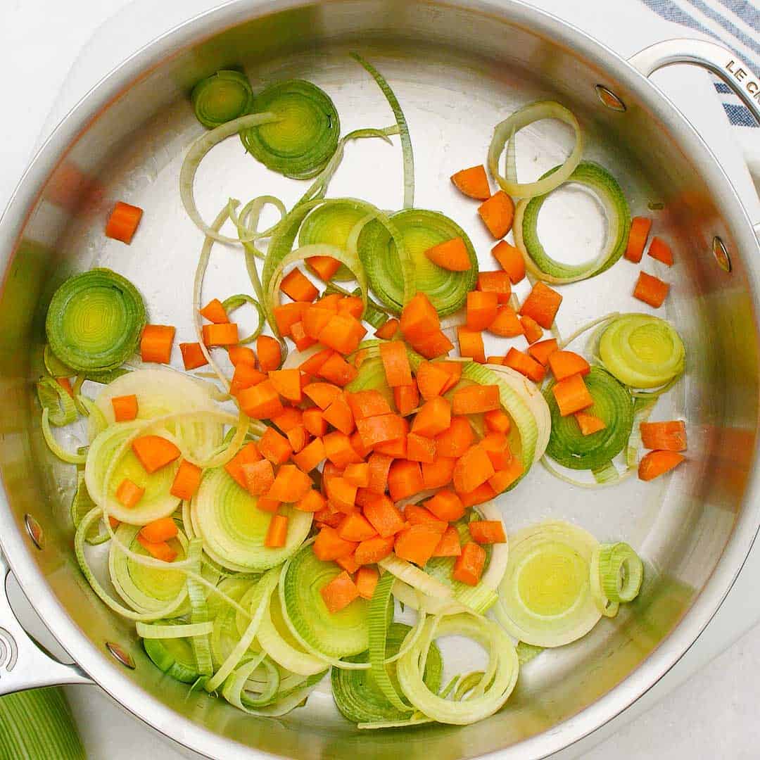Sliced leek and diced carrot in a stainless steel fry pan. 