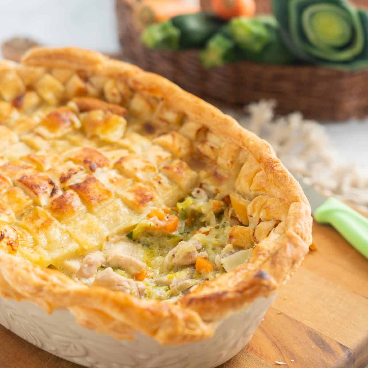 A chicken and leek pie topped with a lattice pastry design, half pastry removed to show the filling. 