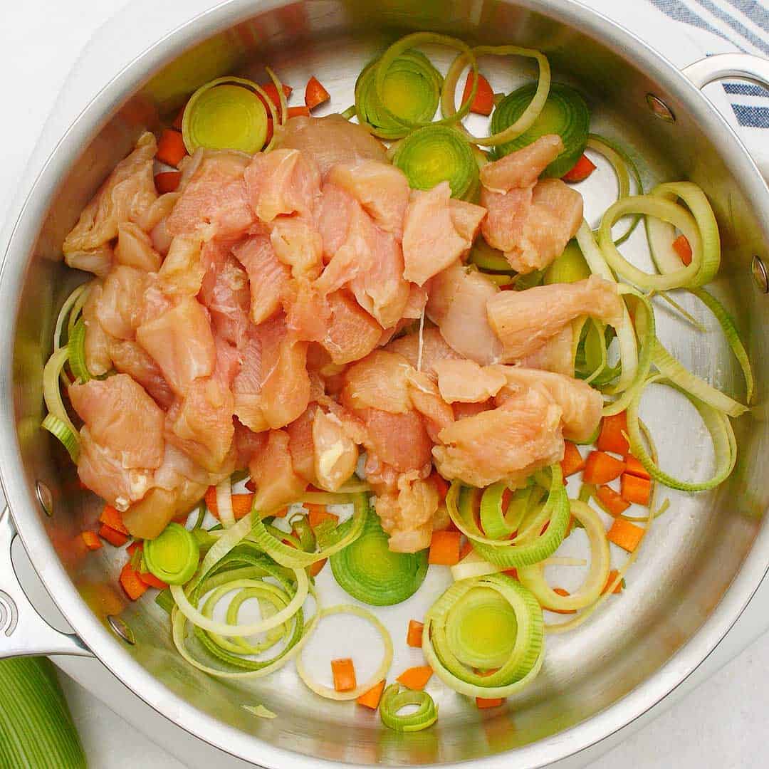 Diced chicken, leeks and carrots in a stainless steel fry pan.