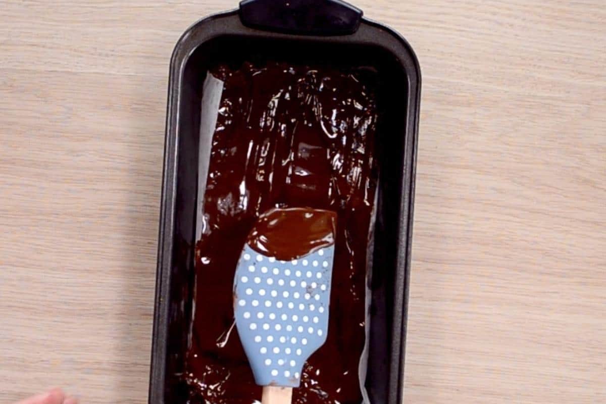 Melted chocolate being spread over a slice with a blue spatula. 