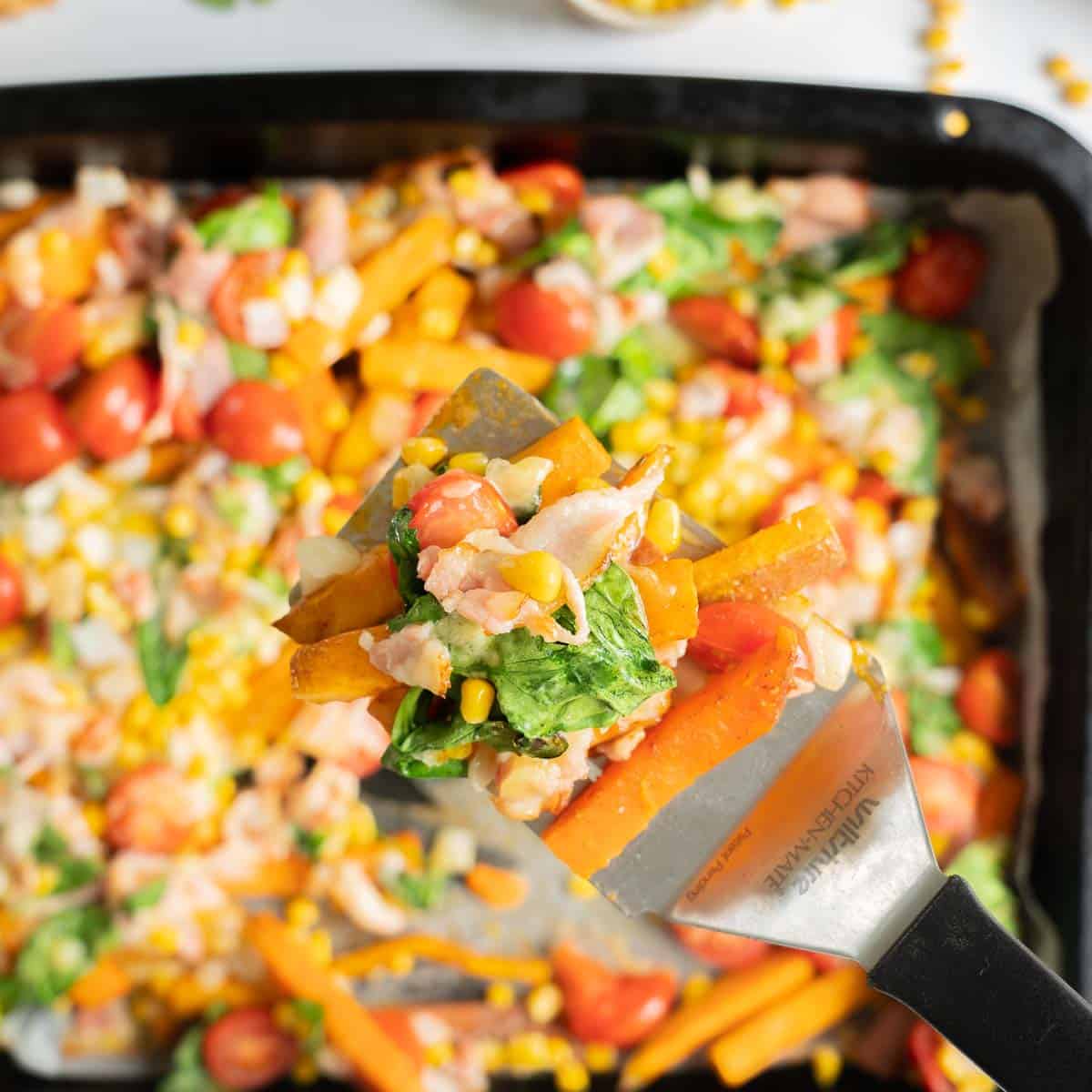 A serving of Loaded kumara fries being held above a tray of colourful vegetables
