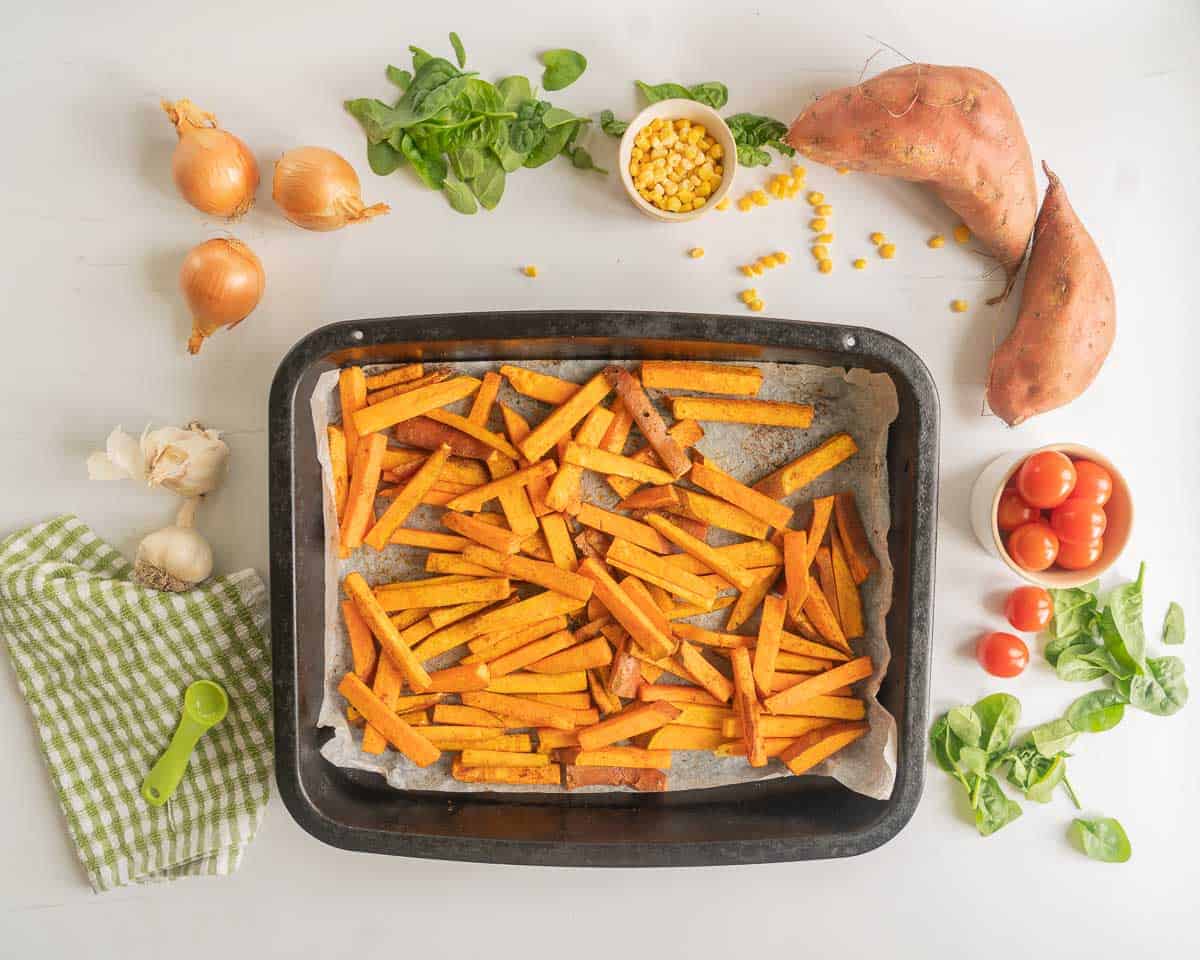 Baked kumara chips in a baking paper lined roasting tin.