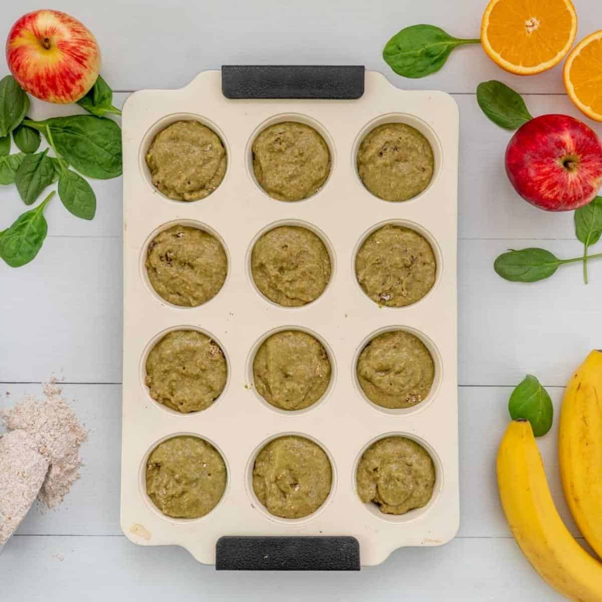 Spinach muffin batter in a 12 cup muffin tray ready to be baked.