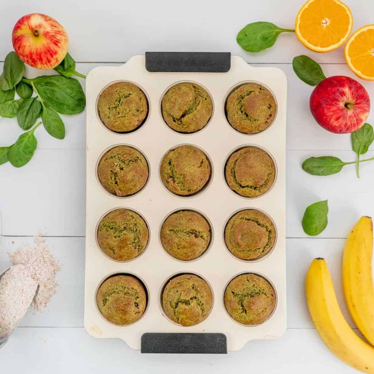 Baked spinach muffins in a cream muffin tray cooling on a bench top.