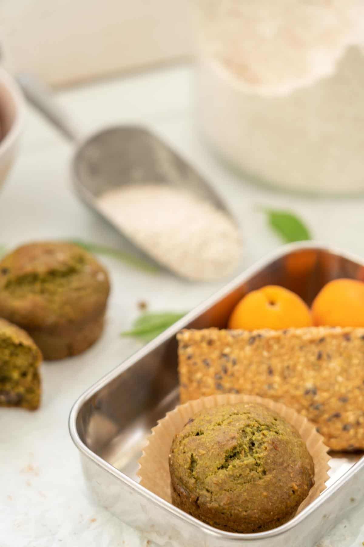 A lunchbox packed with a green muffin, cracker bread and apricots.
