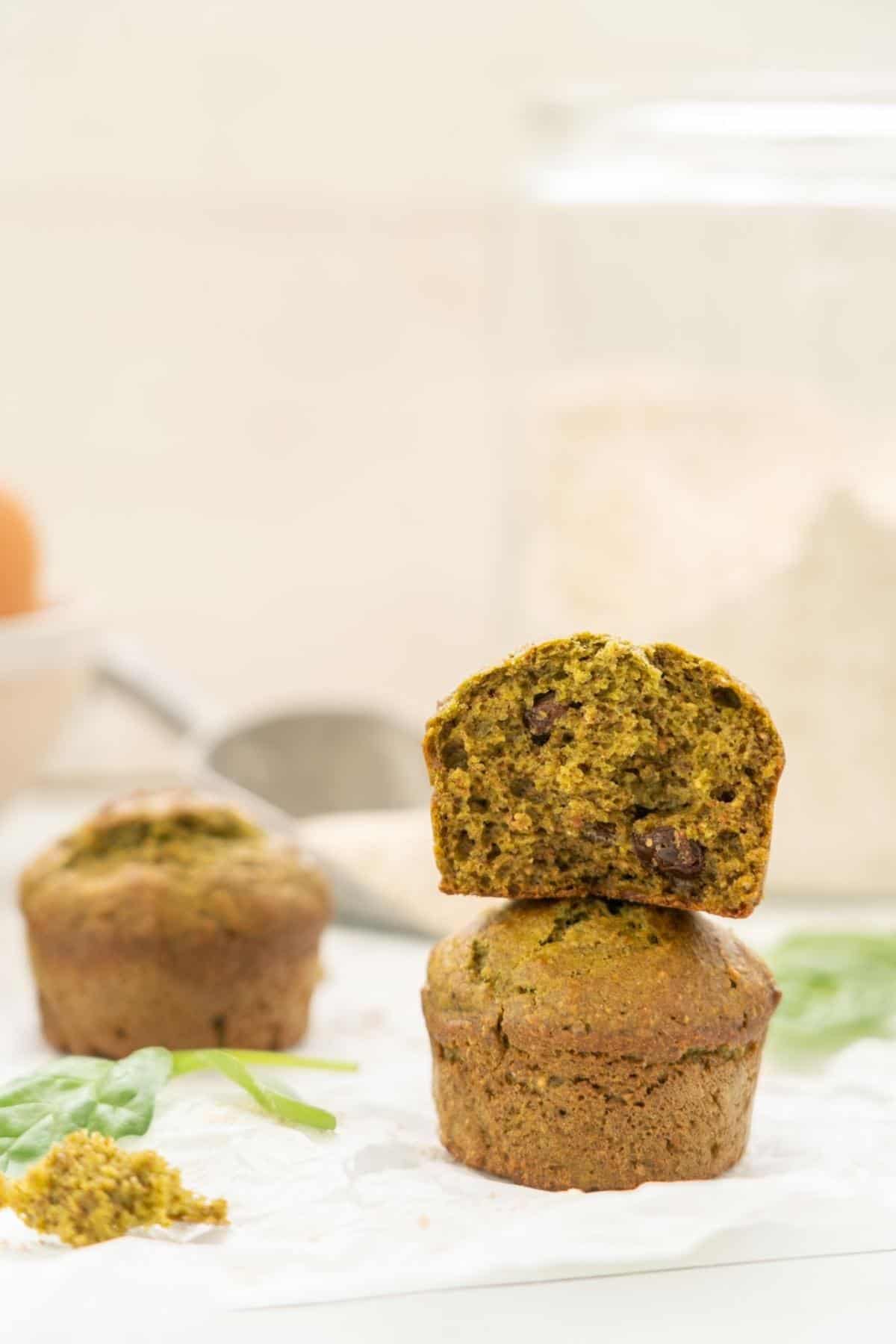 Two spinach muffins stacked on top of each other infront of a large glass jar of flour. 