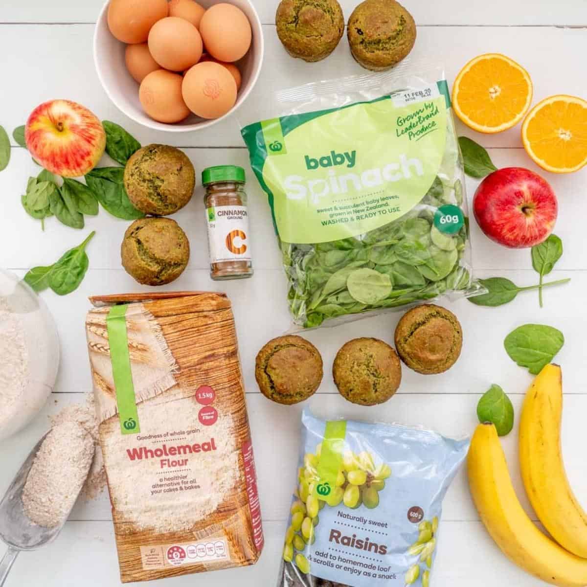 The ingredients to make spinach muffins laid out on a bench top with seven baked spinach muffins. 