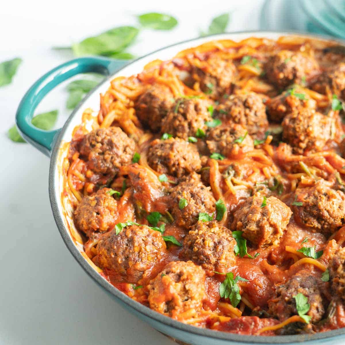 A large green casserole dish fillined with meatballs, pasta and marinara sauce. 