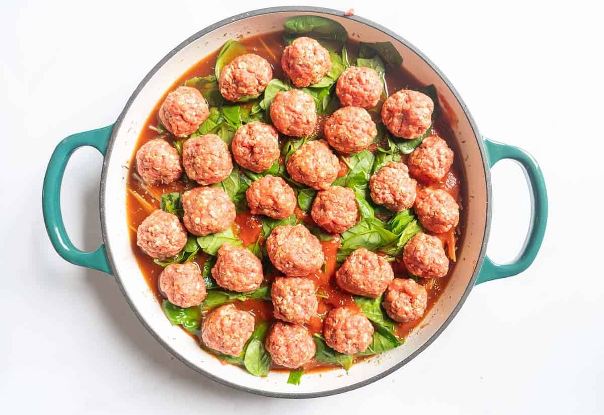 Rolled meatballs on top of tomatoes, pasta and spinach ready to go into the oven. 