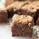 A piece of chocoalte apple cake with crumble topping on a piece of baking paper.
