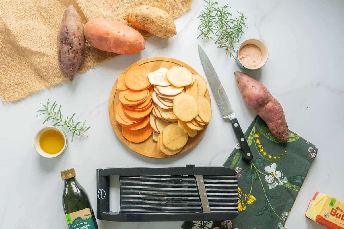 Thinly sliced kumara on a bench top next to a kitchen knife and a mandoline.