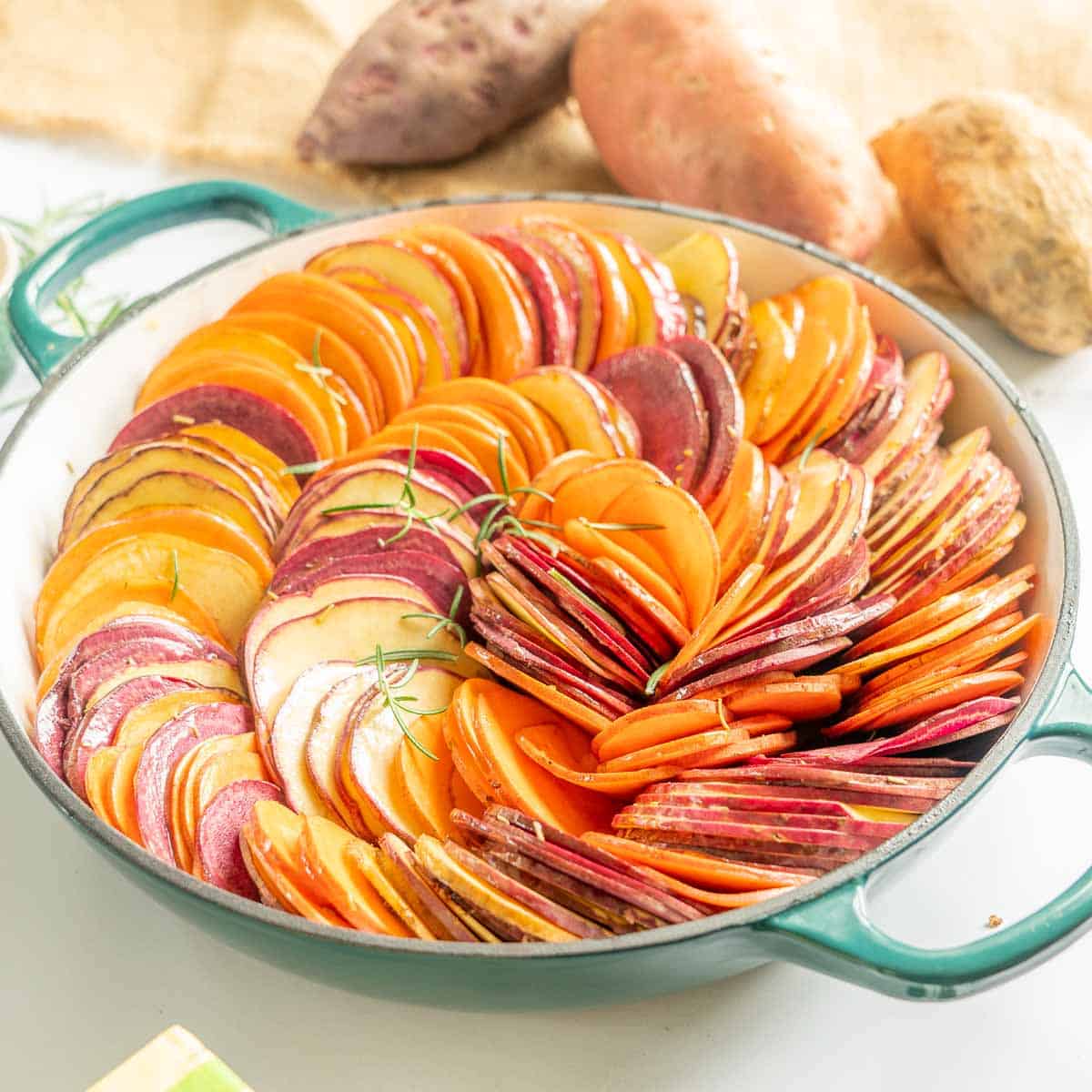 Thinly sliced kumara arranged in a spiral configuration in a round baking dish topped in the butter and rosemary.
