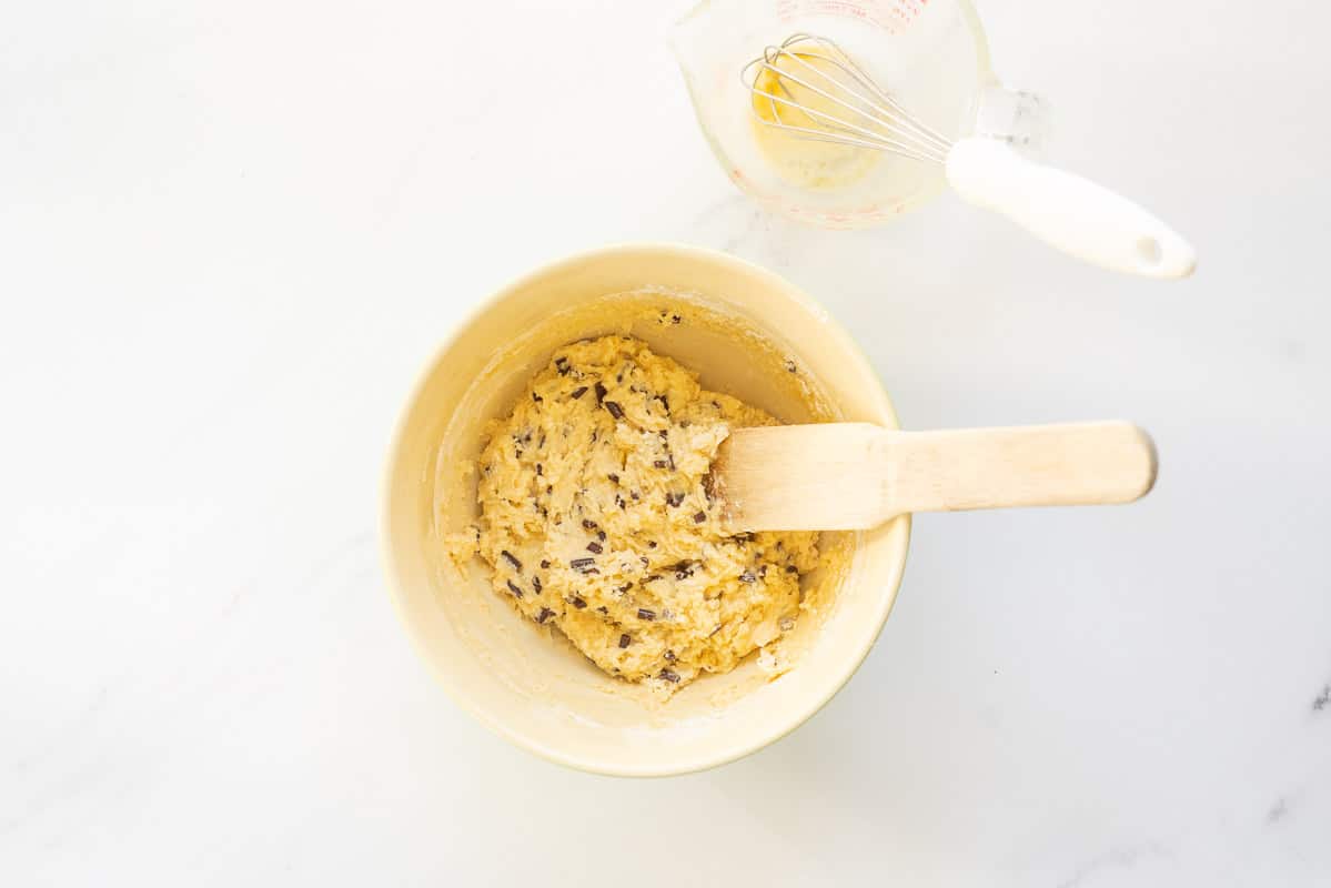 Muffin batter studded with chocolate chips in a ceramic mixing bowl with wooden spoon.
