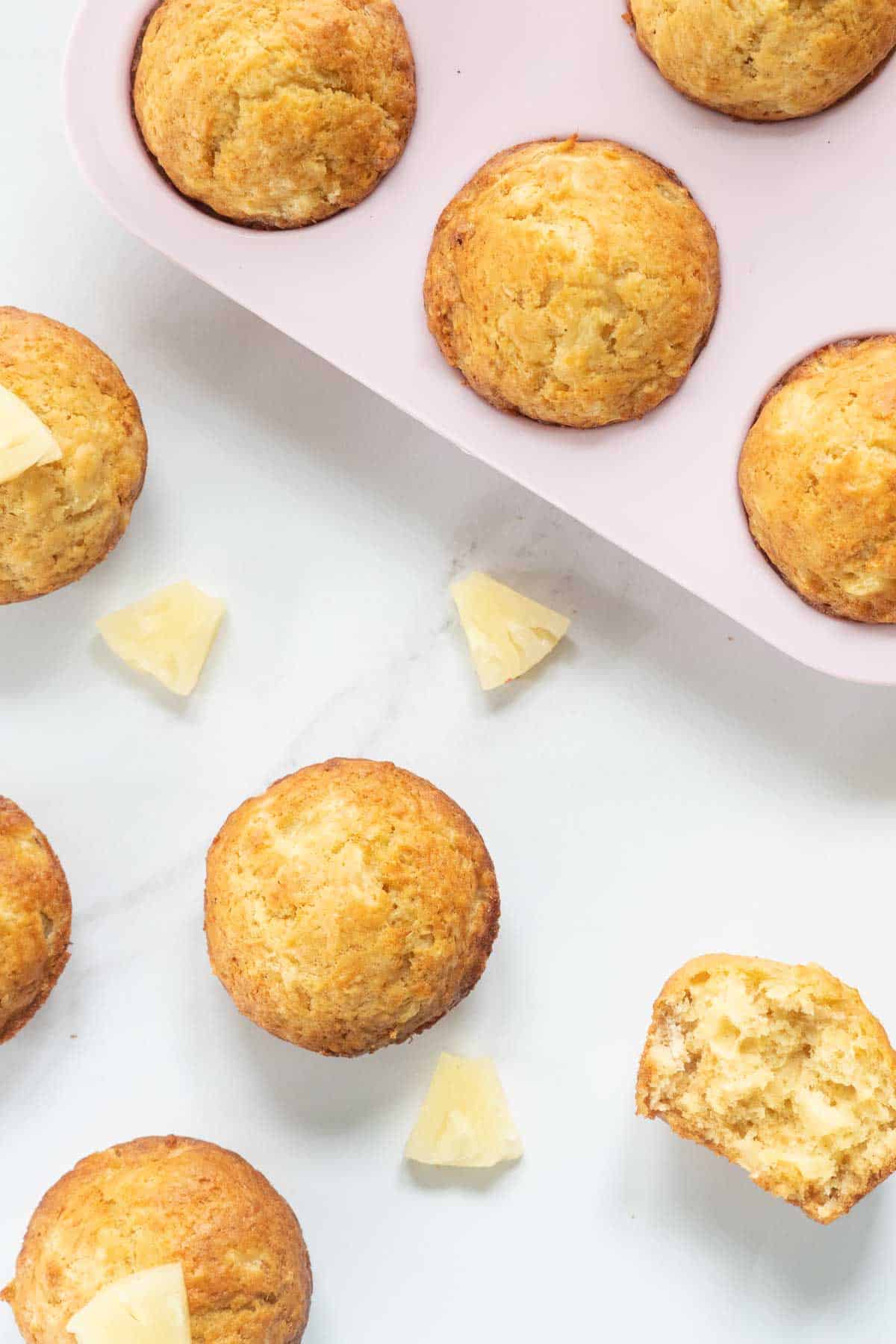 Pineapple muffins on a white marble benchtop scattered with pineapple pieces. 