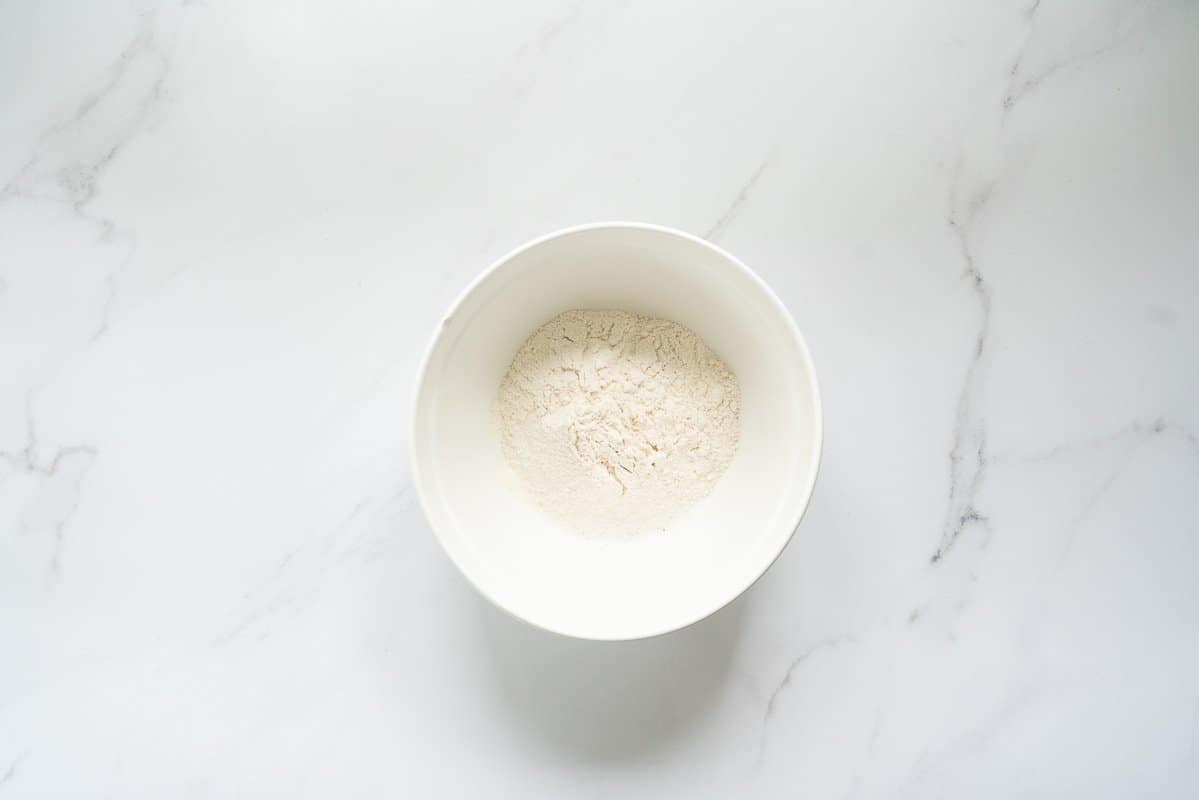A large white ceramic mixing bowl holding dry sifted ingredients.