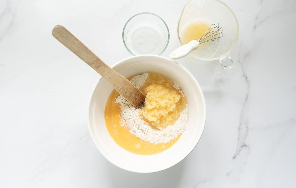A large ceramic mixing bowl filled with flour, whisked eggs and crushed pineapple.
