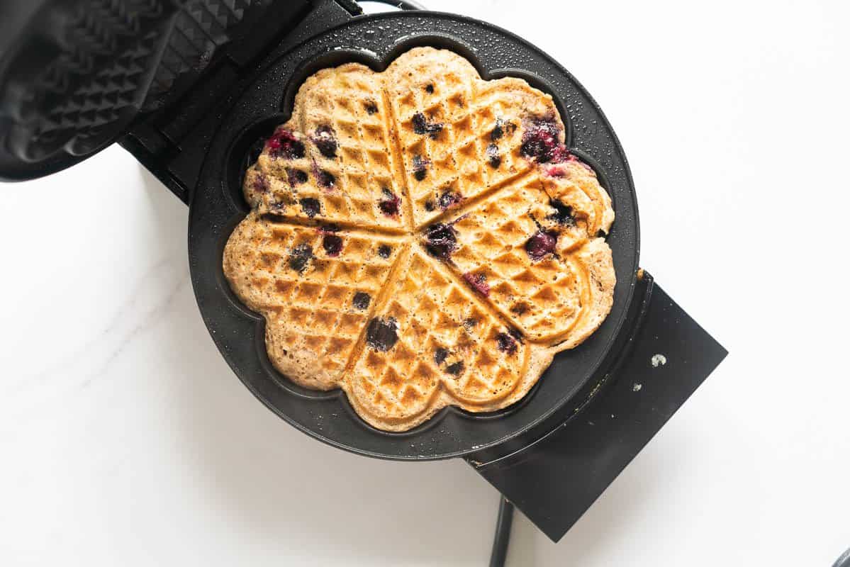 A cooked blueberry waffle sitting in a waffle iron. 