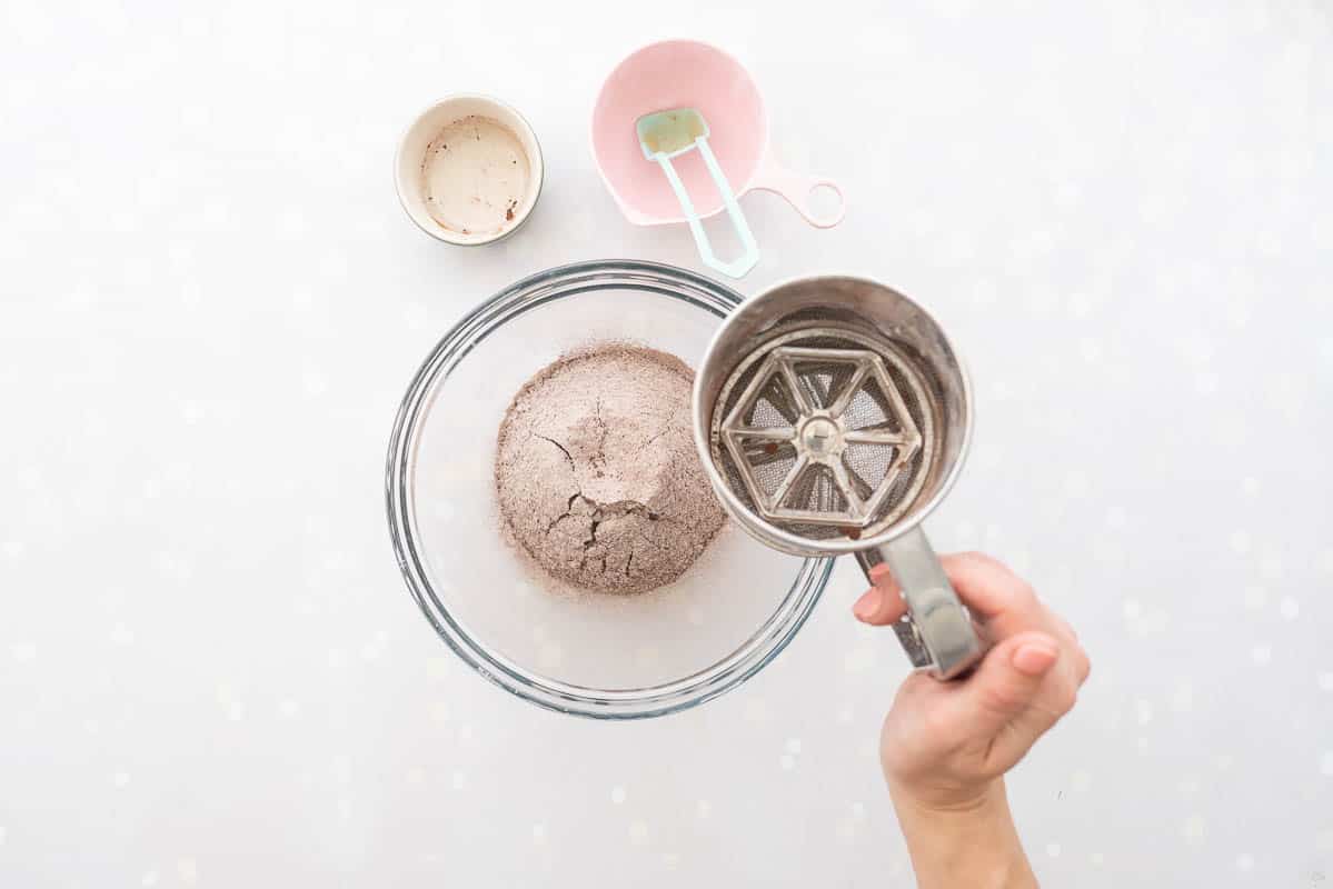 Flour and cocoa powder being sifted into a glass mixing bowl.