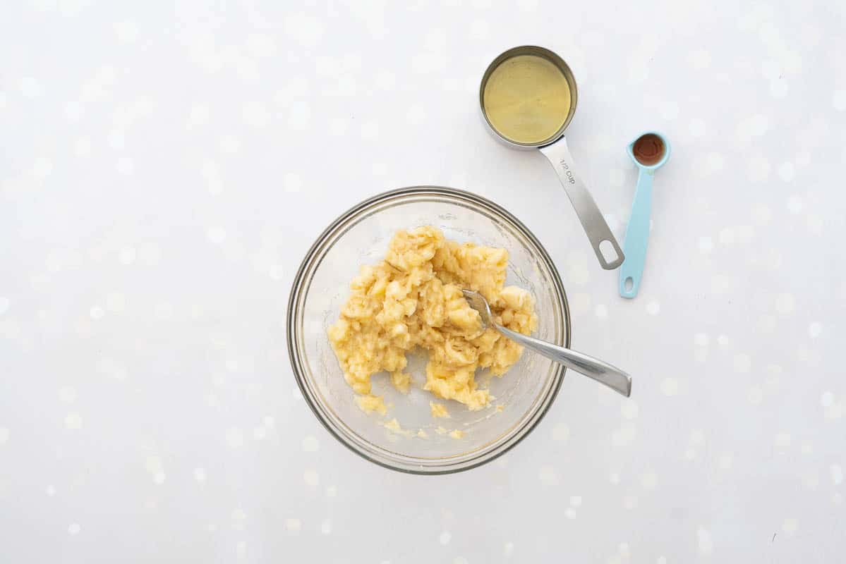 A glass mixing bowl of mashed bananas with a fork resting in it.