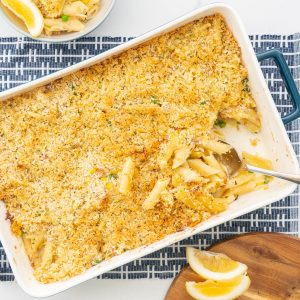 Crunchy topped tuna pasta bake sitting on a blue placemat with a large serving spoon.