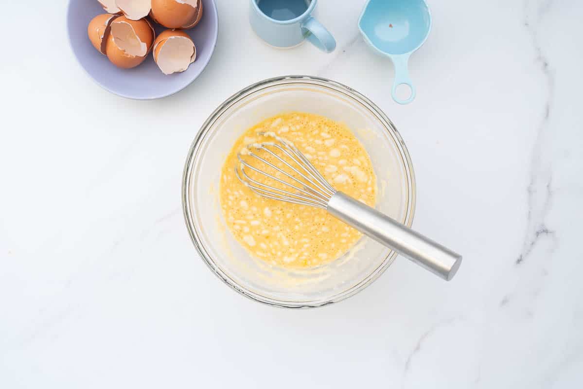 A mixing bowl containing an egg batter, lumps of flour visible. 
