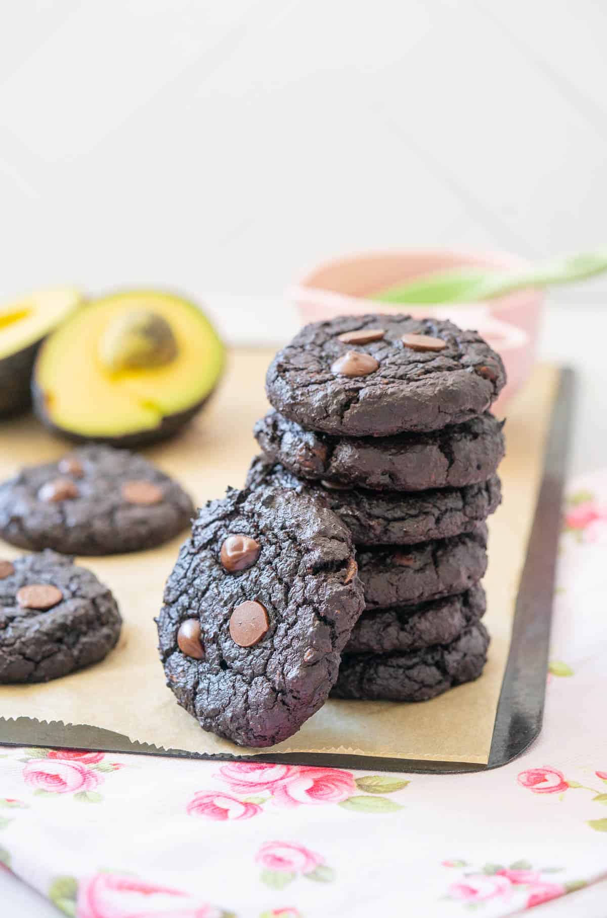 A stack of 7 chocolate cookies on a pink floral tea towel with an avocado in the background