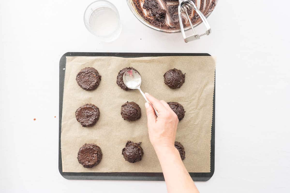 Chocolate avocado cookies being shaped using the back of a spoon.