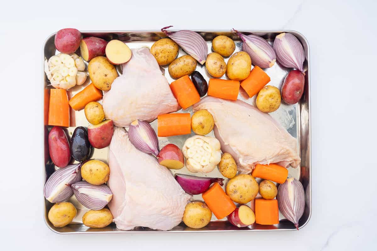 Vegetables and three chicken breasts in a large stainless steel tray.