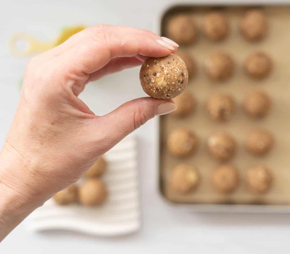 A banana bread energy ball being held above a tray of more balls.