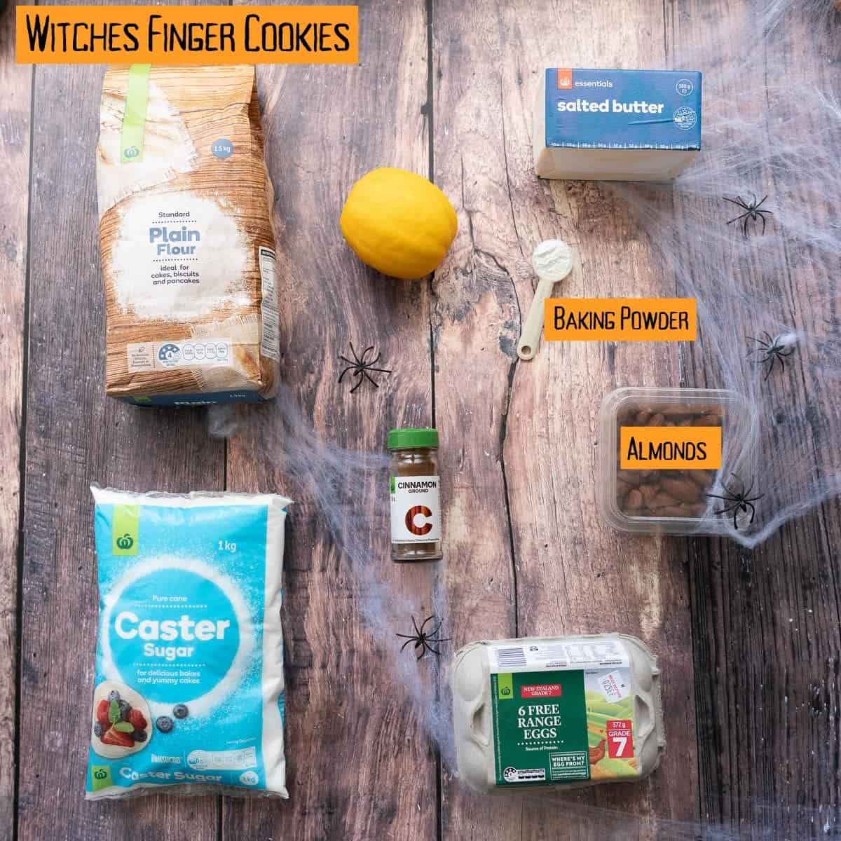 The ingredients to make witch finger cookies laid out on a dark wooden table top with text overlay.
