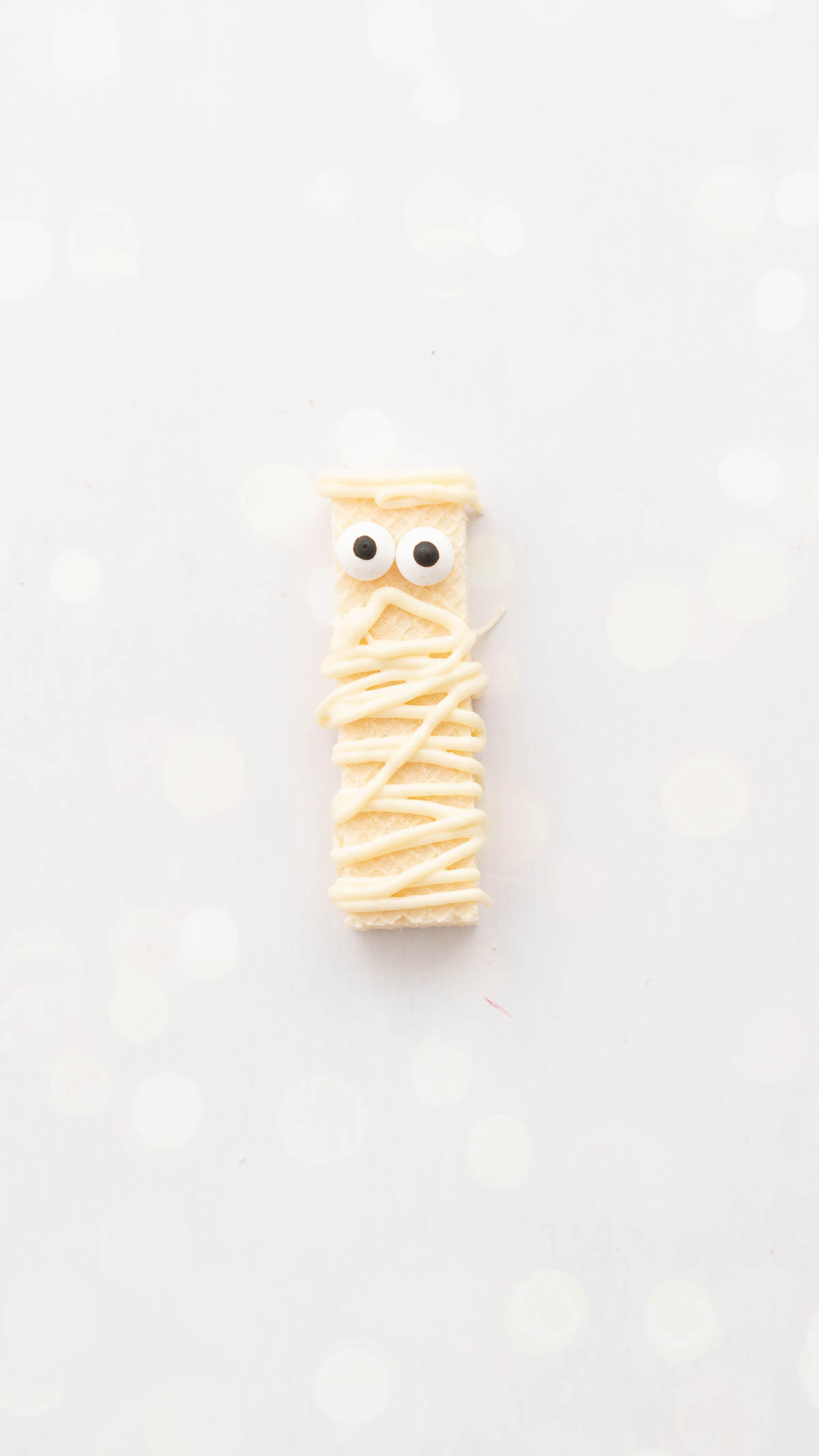 A cookie decorated as a mummy sitting on a bench top.