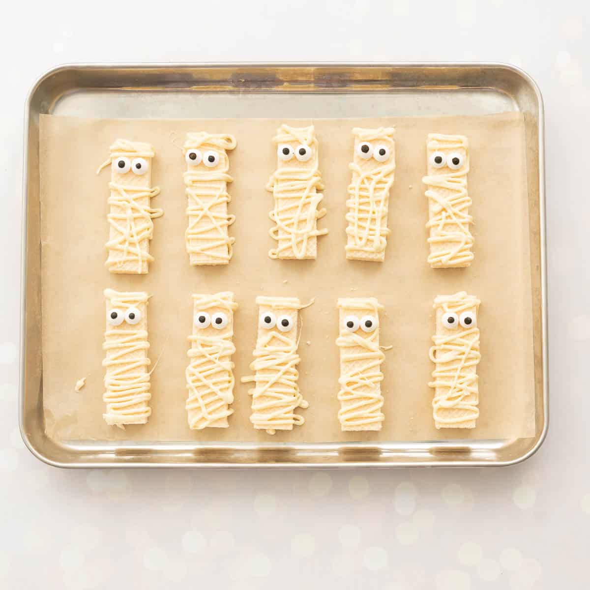 Ten wafer biscuits decorated to look like mummies with melted white chocolate and candy eyes