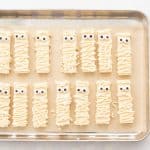 Cookies decorated as Mummies for Halloween on a lined baking tray.